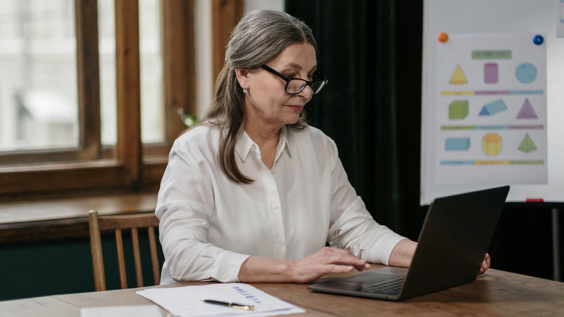 Elderly woman focused on her work with a laptop and documents in an office.