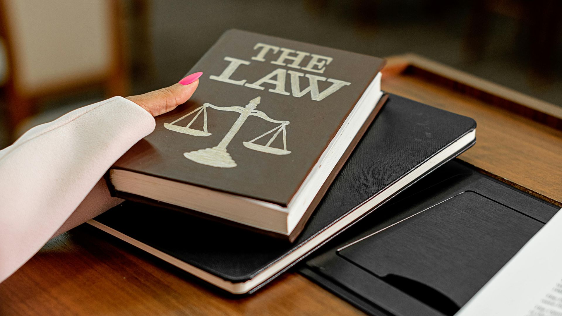 Closeup image of a law book titled 'The Law' on a wooden desk with scales of justice.