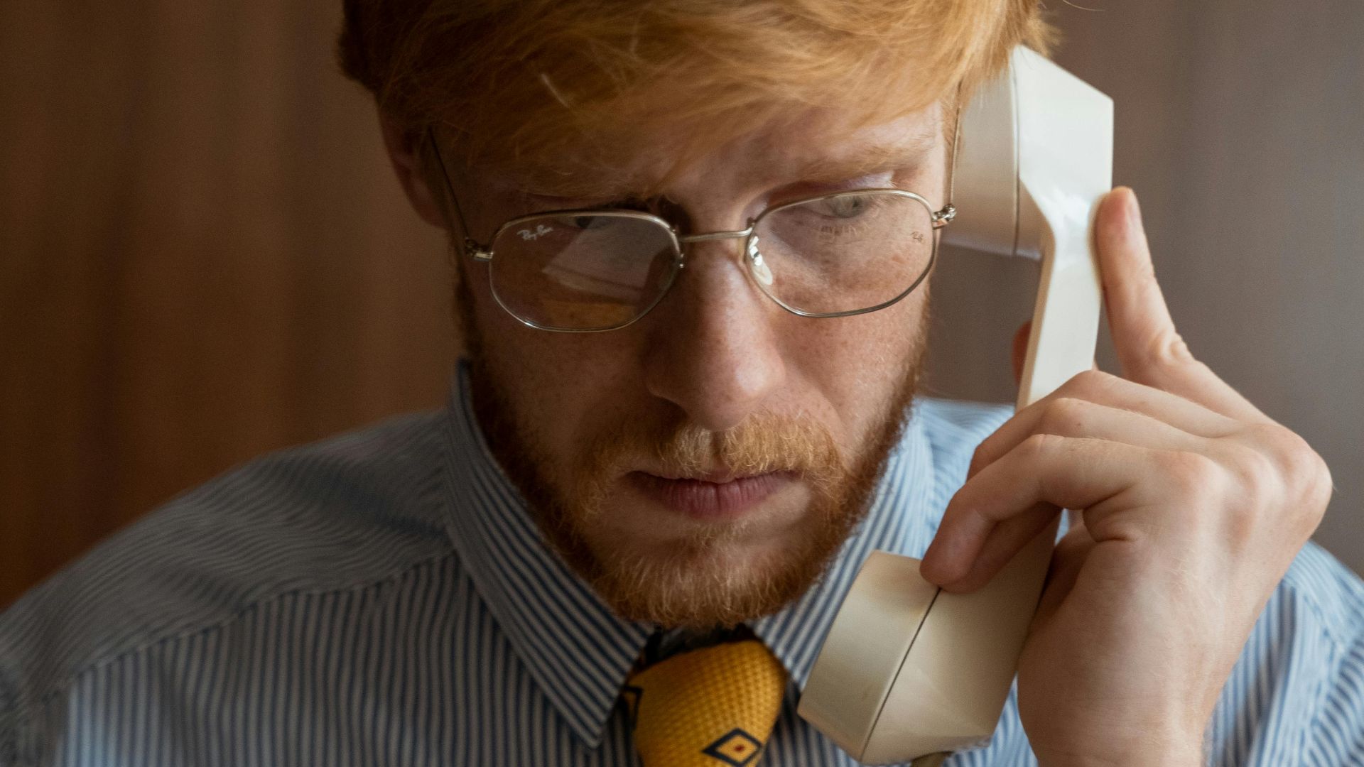Businessman with a yellow tie conversing on a vintage landline phone in an office.
