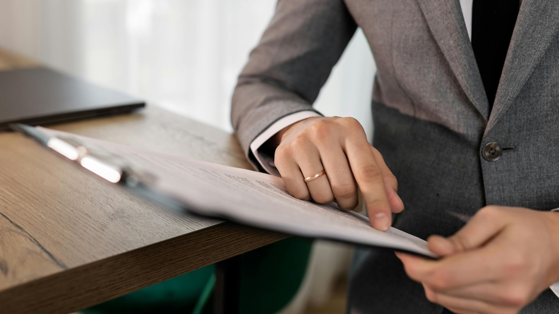 Professional businessman in suit reviewing documents on clipboard at office desk.