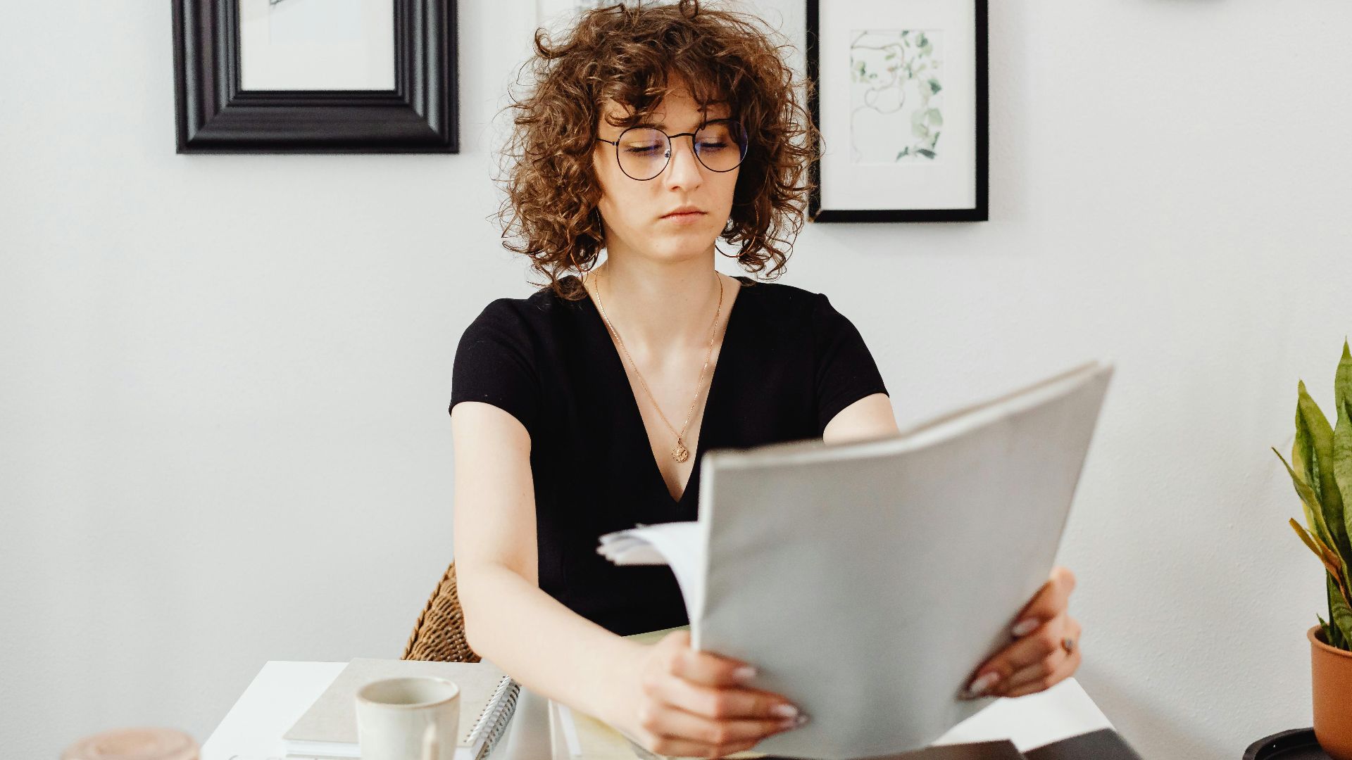 Woman with curly hair and eyeglasses reviewing documents at her desk.