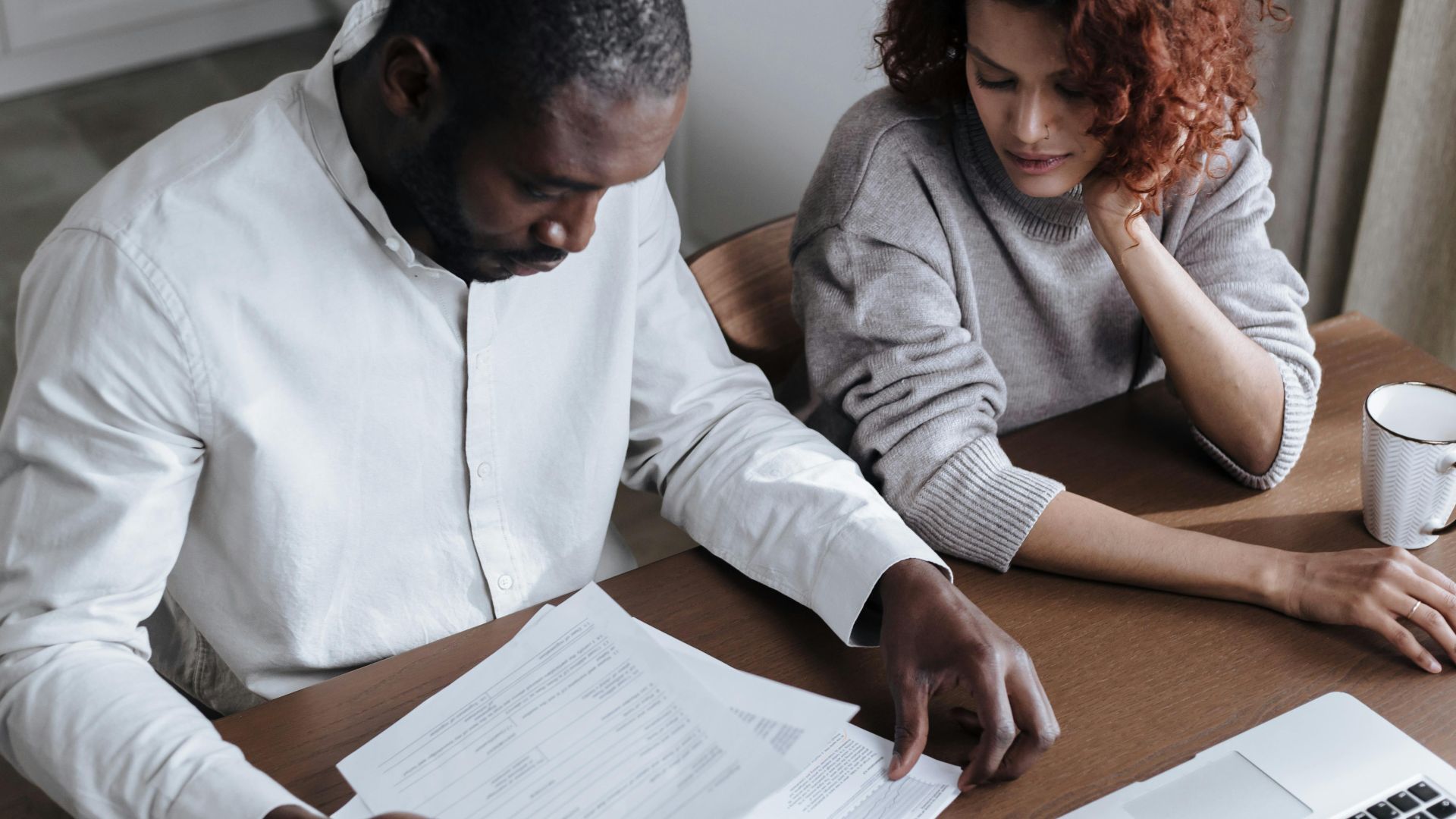 A couple reviews important documents together at a home desk with a laptop.