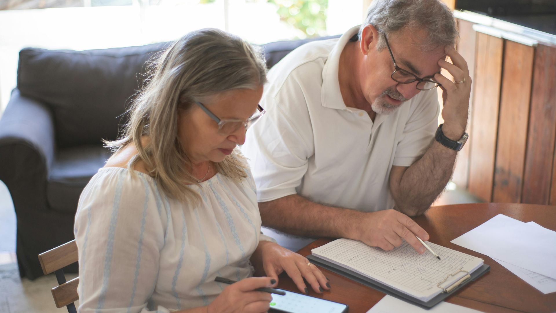 Elderly couple reviewing bills and documents at home, focusing on finances and technology.