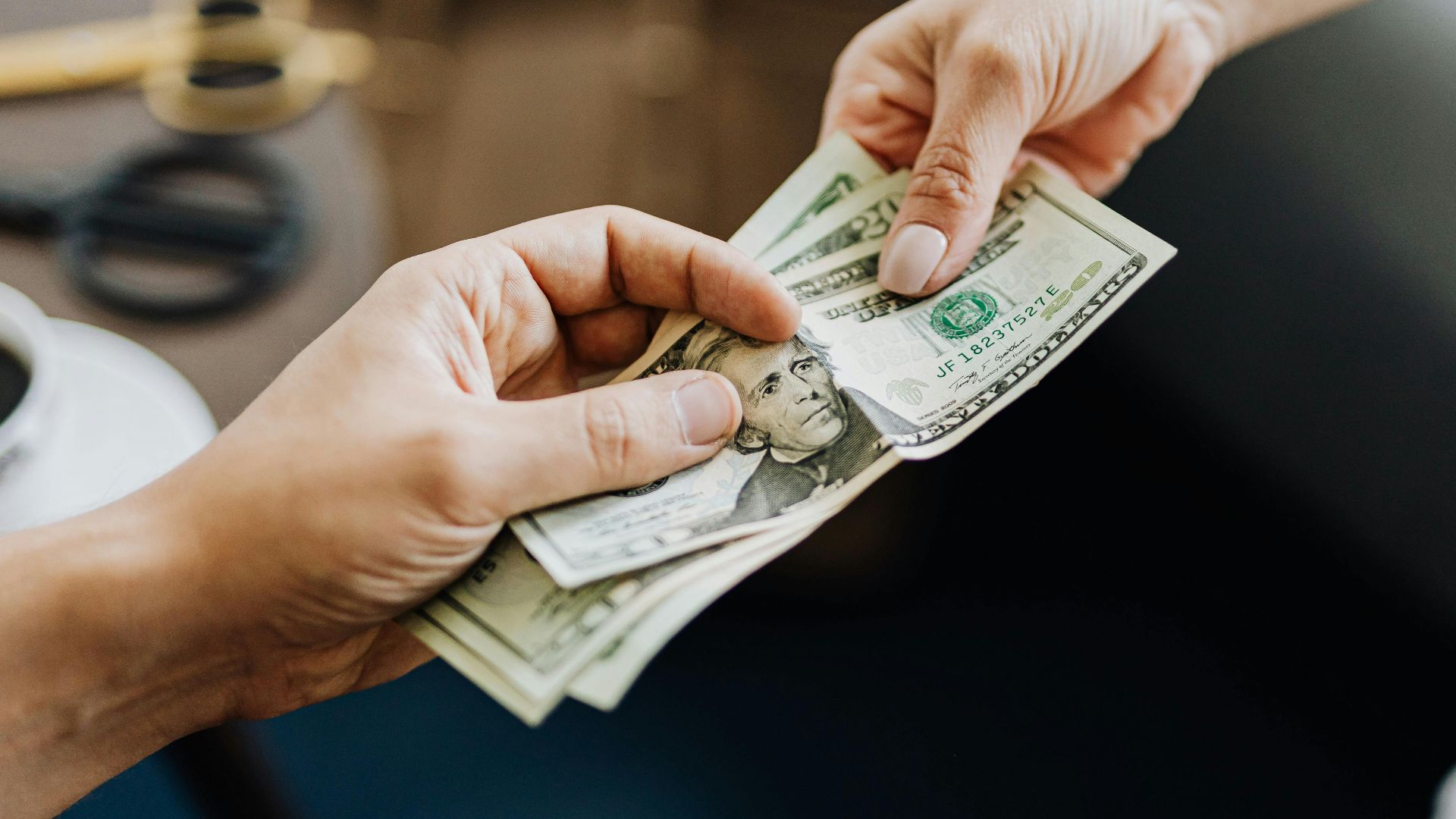 A close-up image of hands exchanging US dollar bills, symbolizing financial transaction or payment.