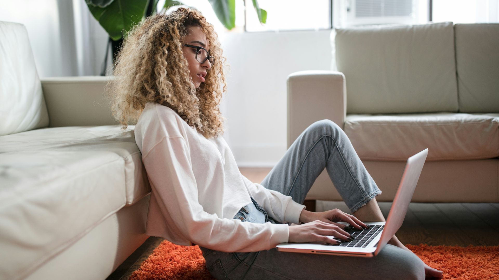 woman sitting on floor and leaning on couch using laptop