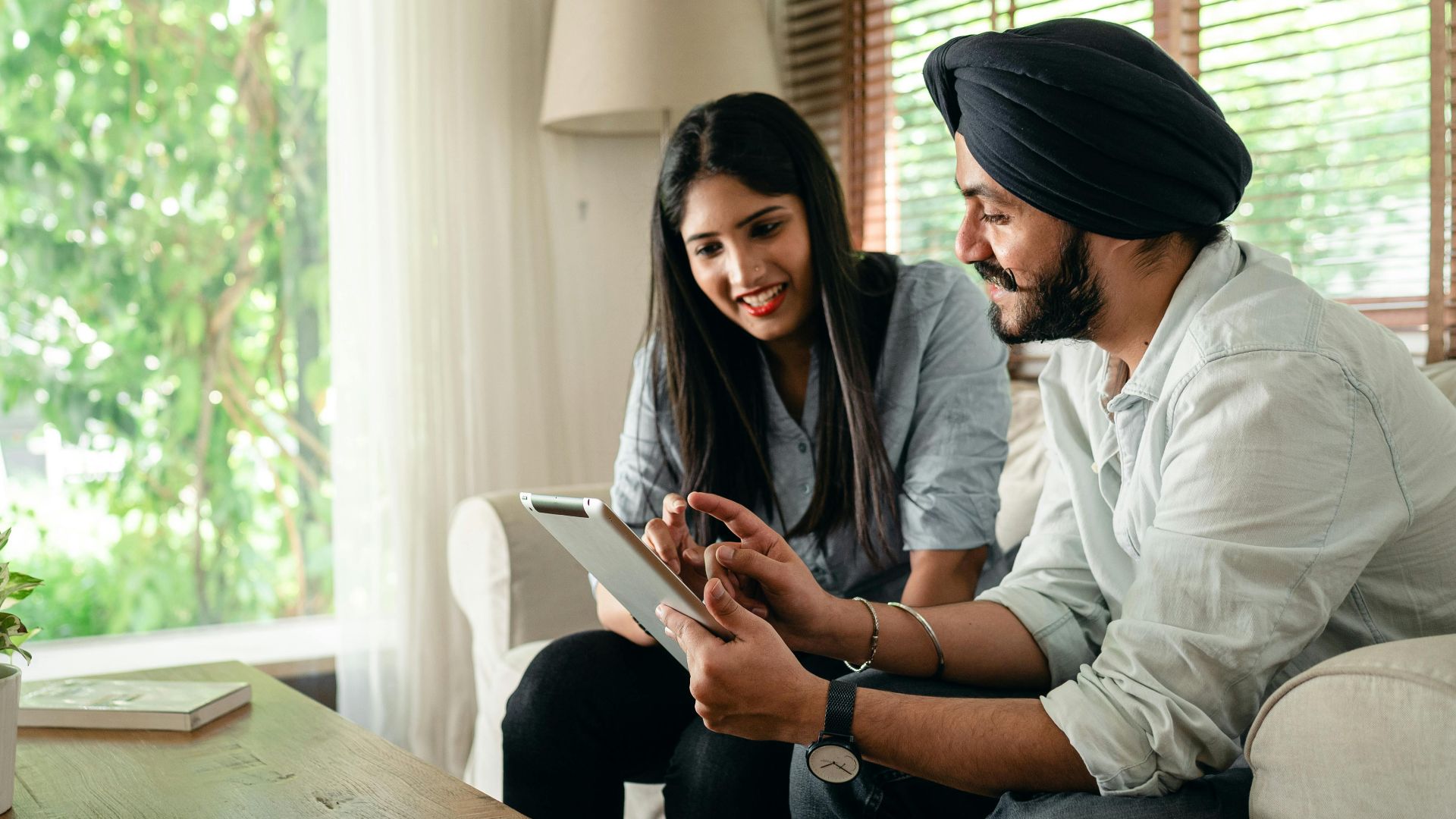 Young Indian man in casual outfit and turban working on project with female colleague using tablet in cozy workplace