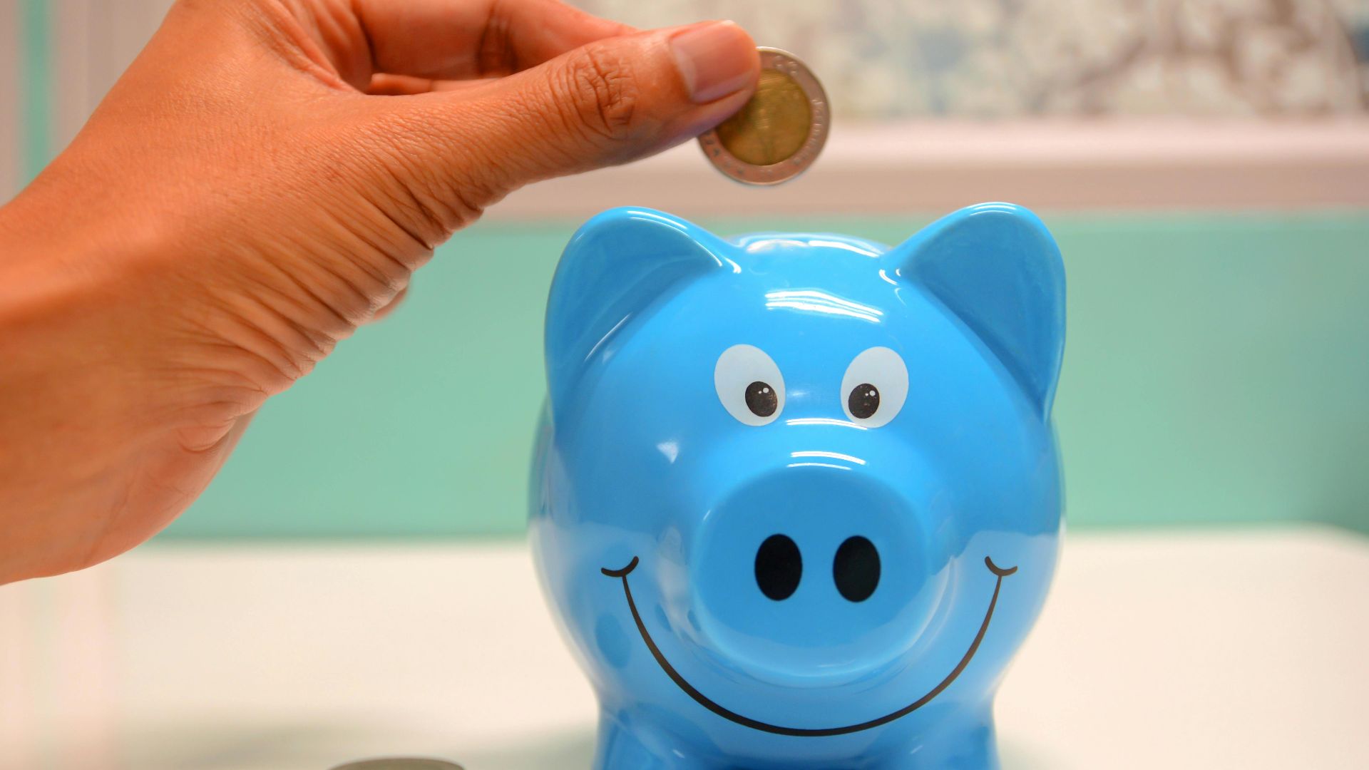Hand inserting a coin into a blue piggy bank for savings and money management.