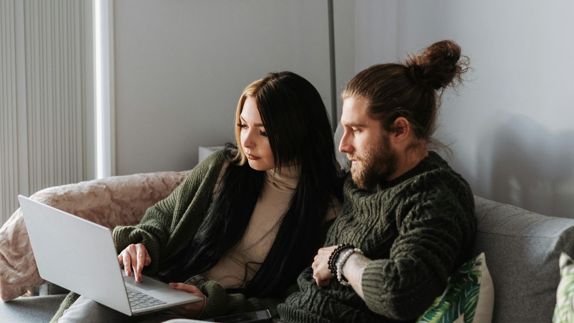 Young woman with hipster boyfriend browsing internet on netbook while resting on soft couch at home