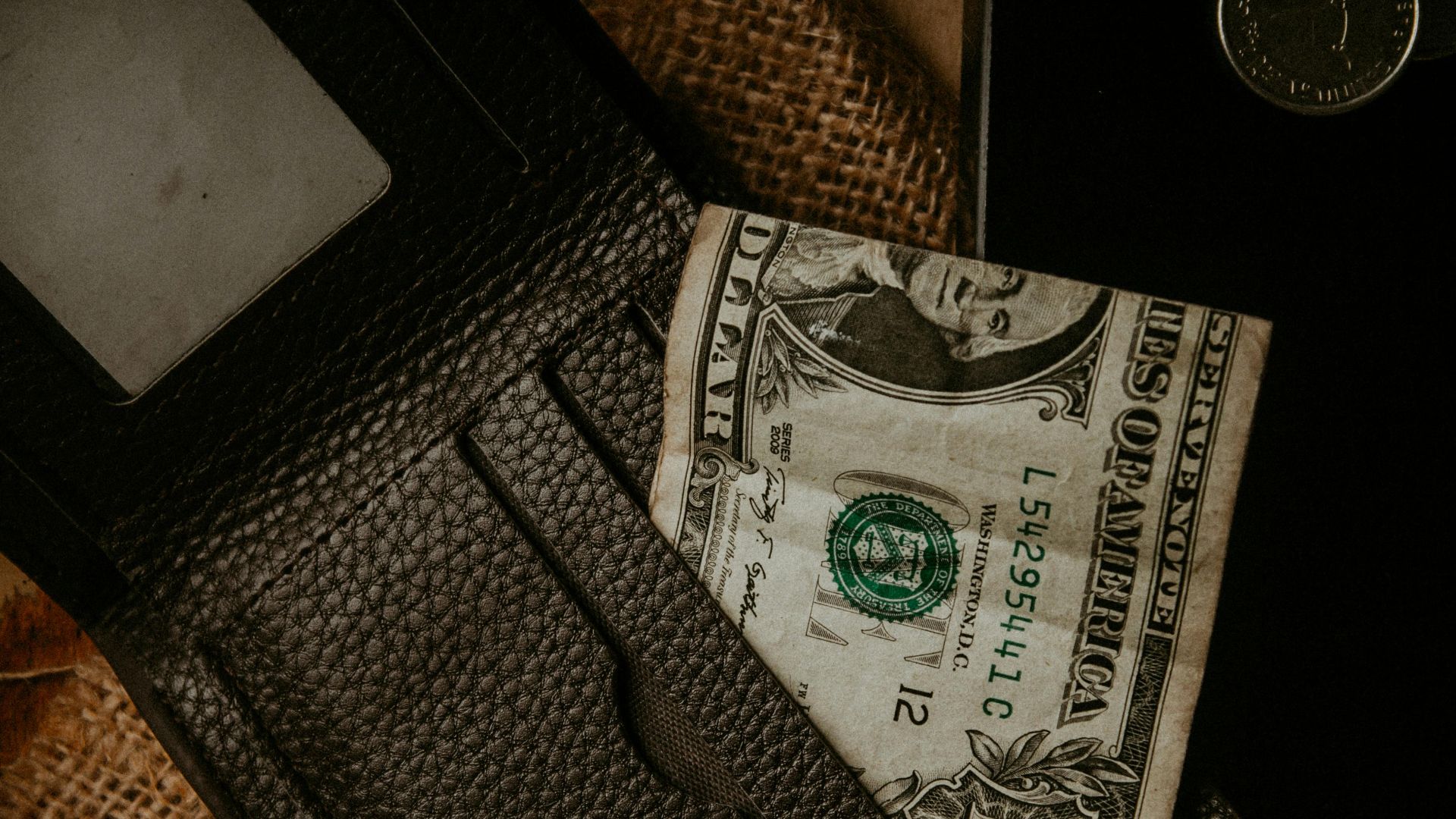 A close-up view of a leather wallet with a one dollar bill and coins, highlighting personal finance concepts.