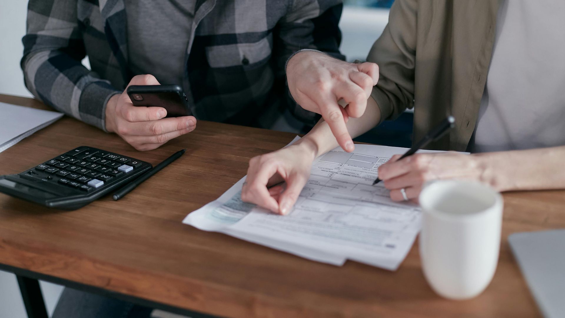 A couple analyzing financial documents and using a calculator at a home table.