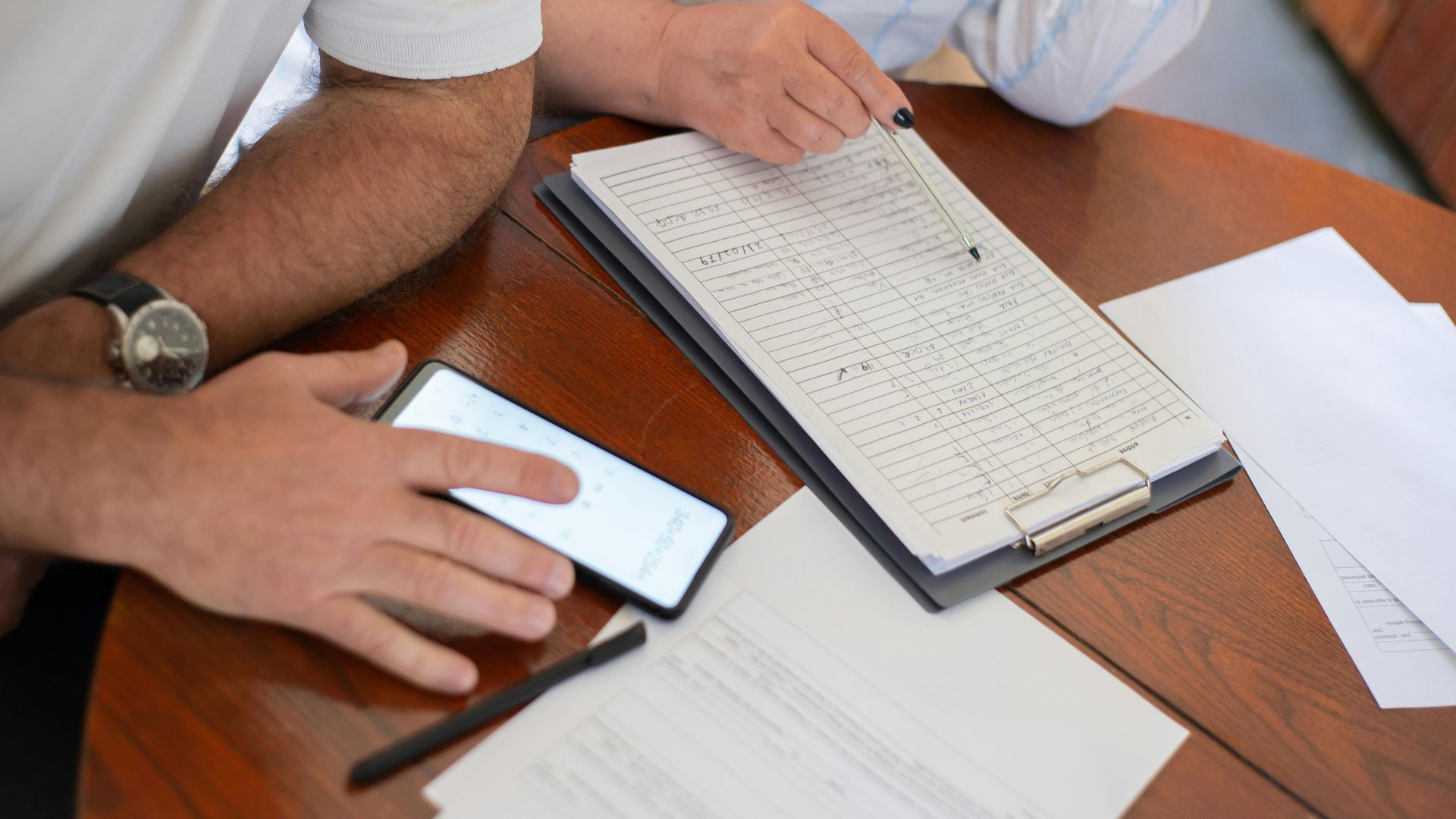 Senior couple examining bills and documents with smartphone and clipboard at home.