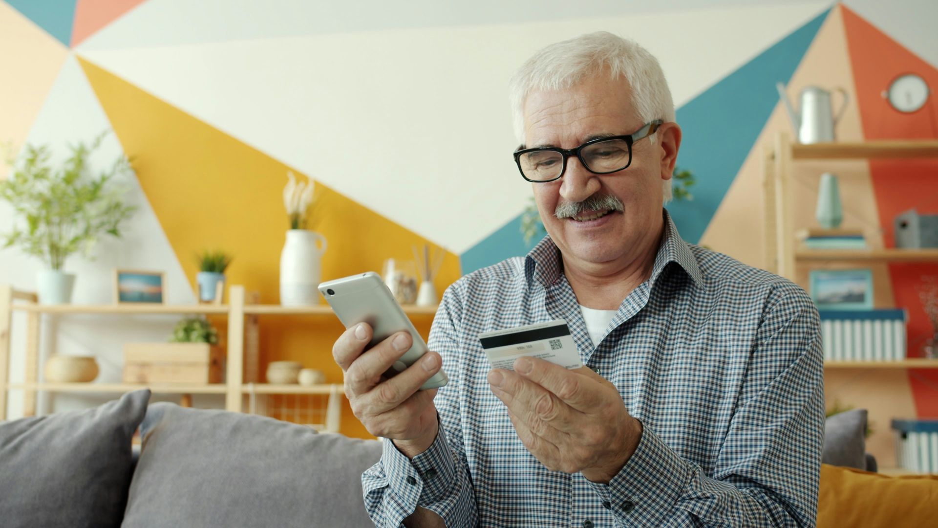 Elderly man uses smartphone and credit card for online shopping.