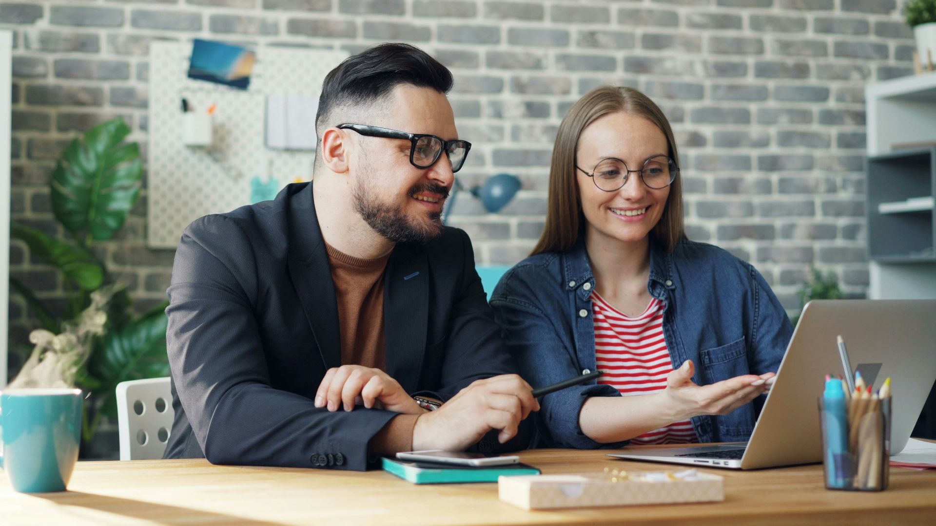 a man and a woman sitting at a table looking at a laptop