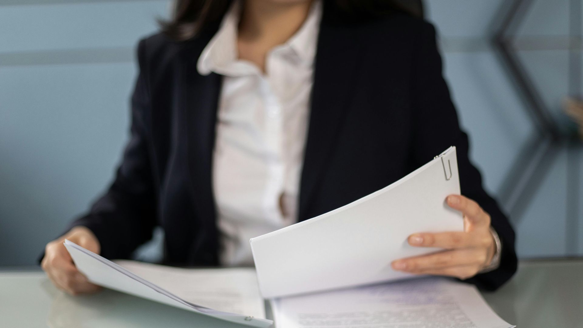 Businesswoman in formal attire reviewing and organizing documents at an office desk.