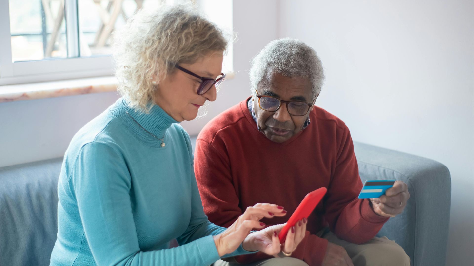 Elderly couple using a smartphone for online shopping, holding a credit card.