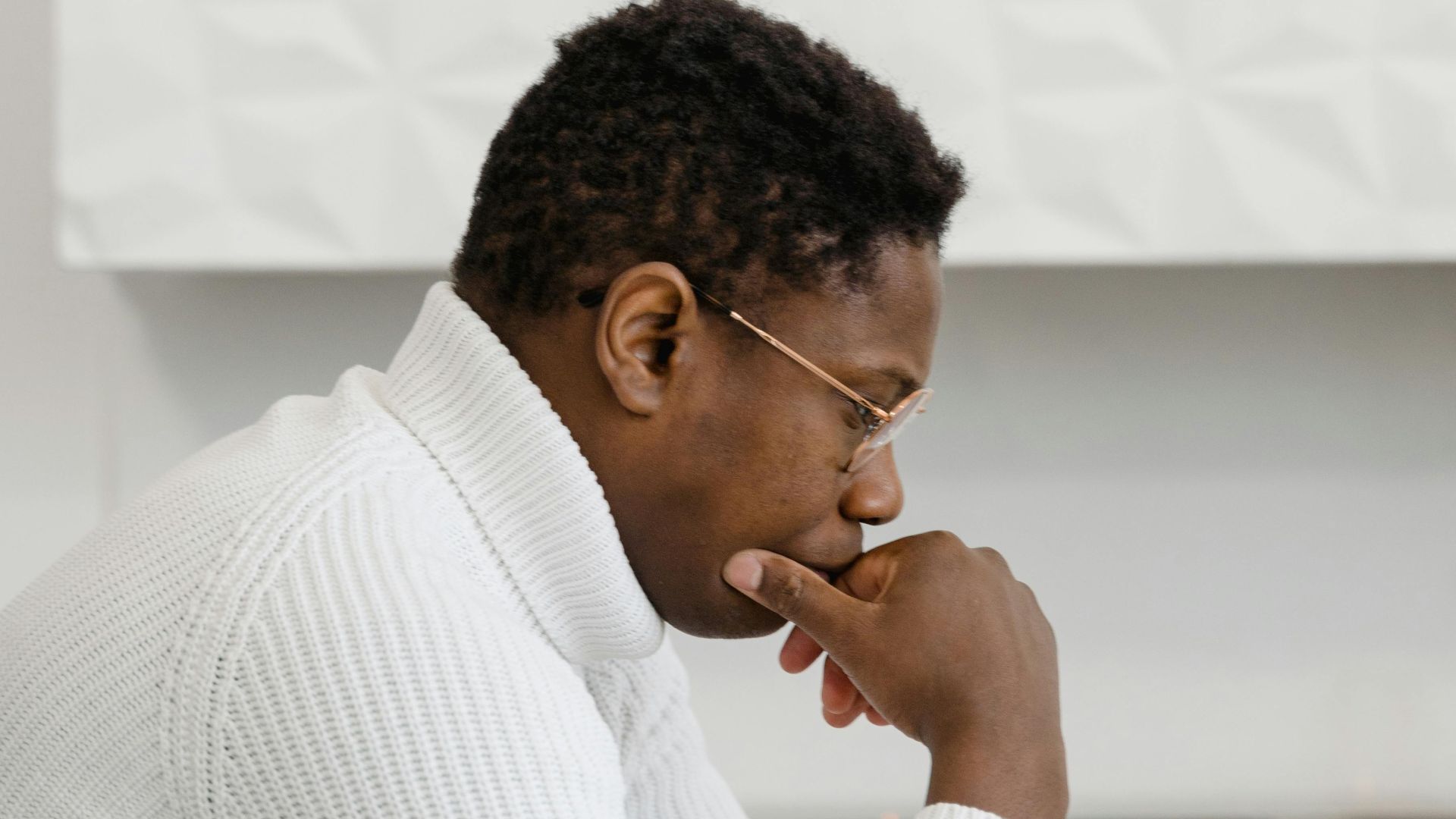 Side view of a man in deep thought, sitting indoors against white walls.