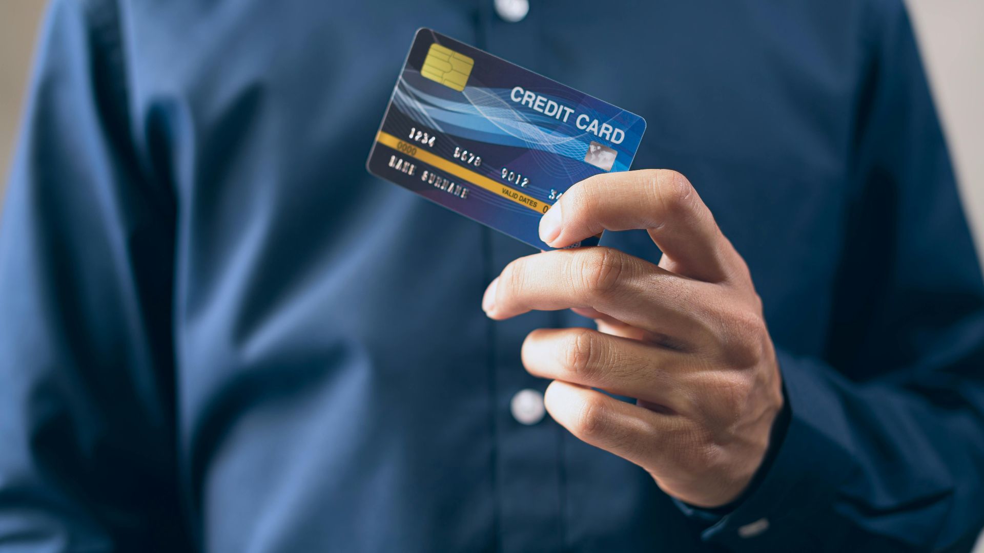 Close-up of a person holding a credit card in a hand, wearing a button-up shirt.