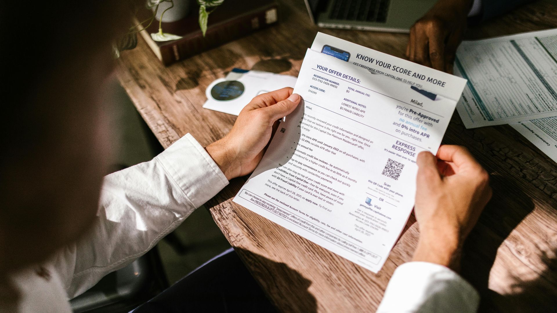An adult man examining a financial document under natural light at a wooden desk, emphasizing finance and reading.