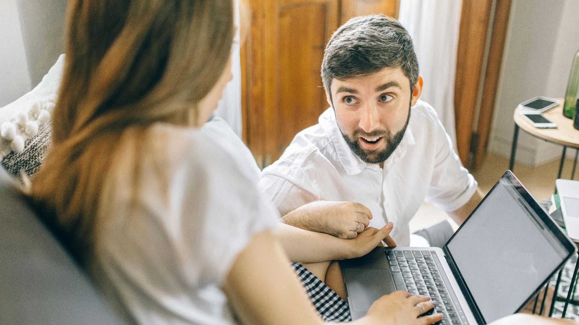 Couple working together from home on laptops, engaged in conversation.