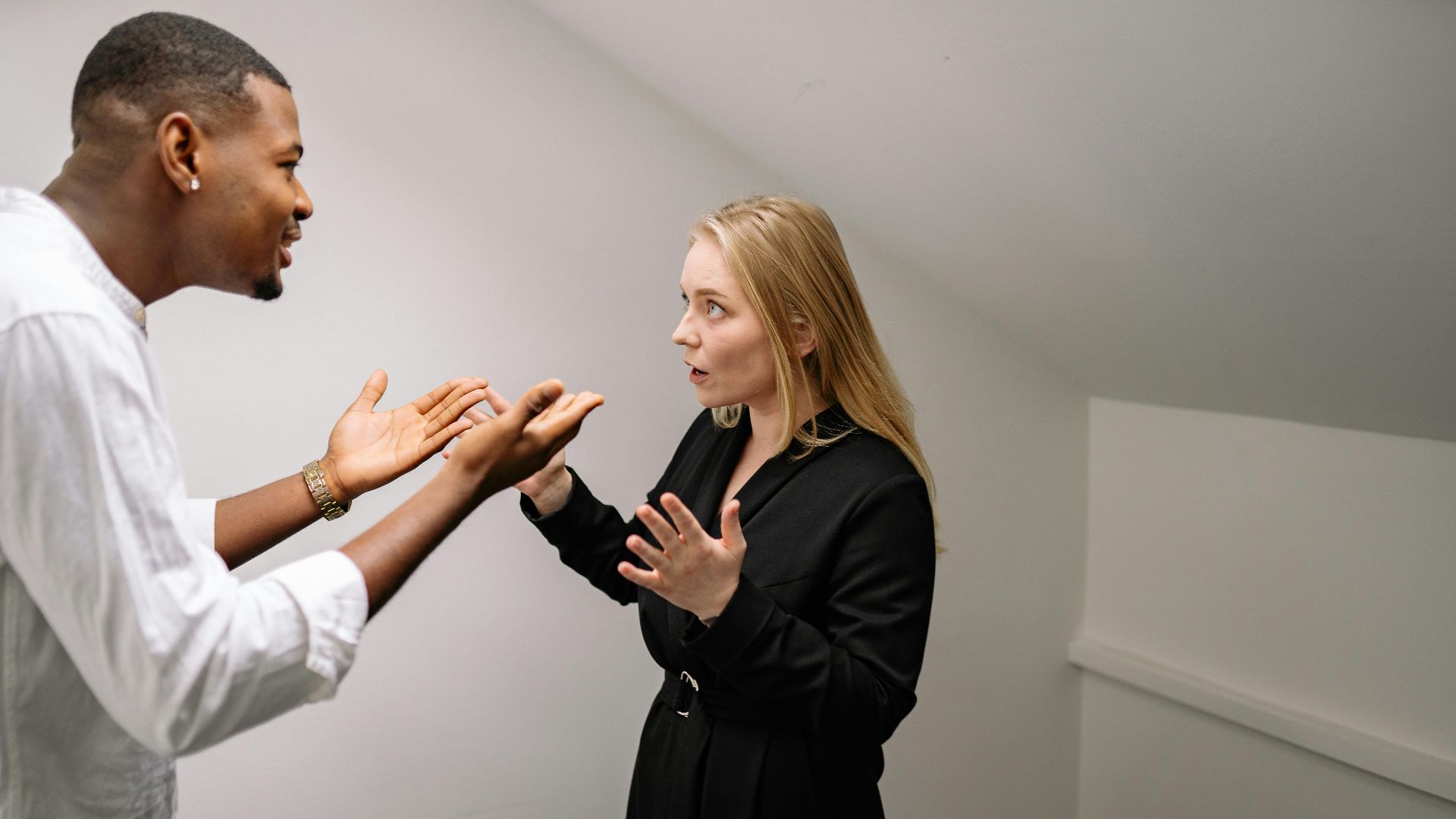A man and woman having a heated discussion in a minimalistic indoor space.