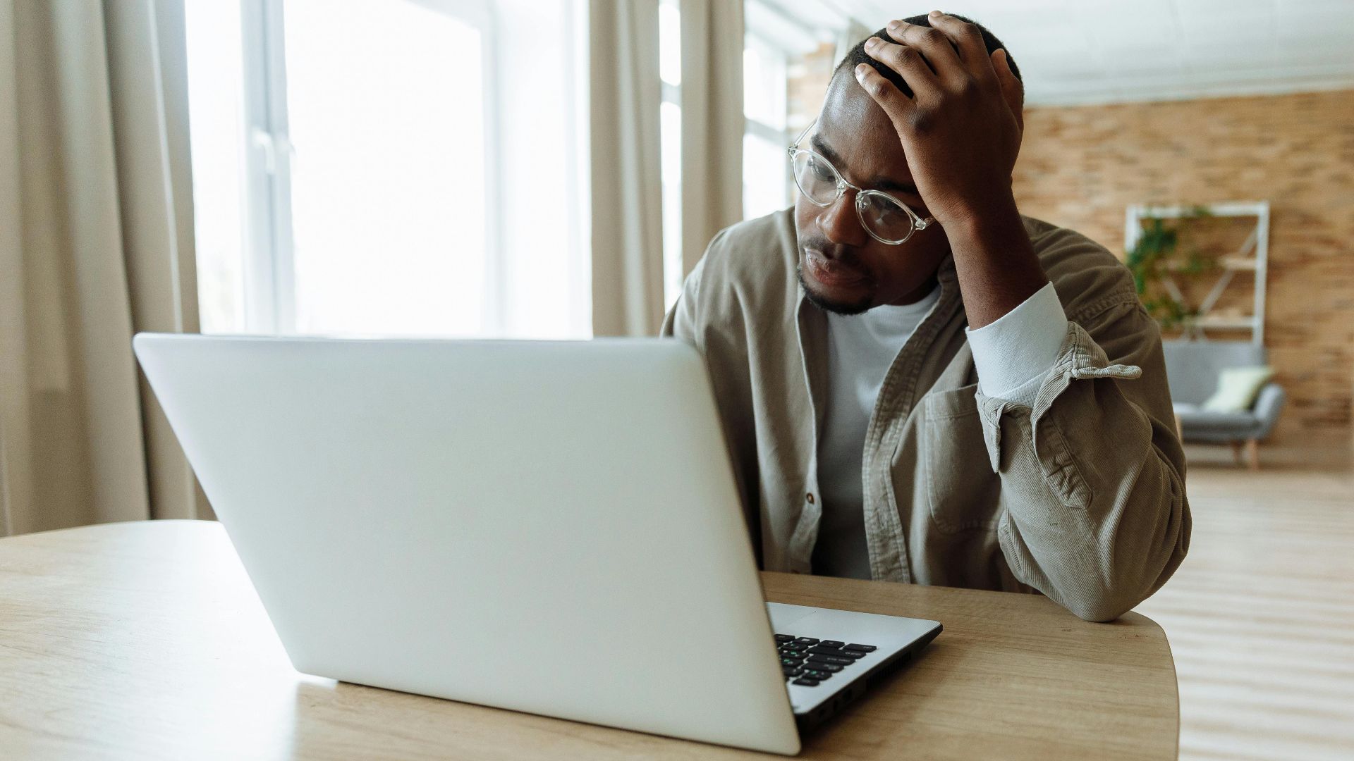 Man stressed while working on a laptop indoors, dealing with issues in remote work.
