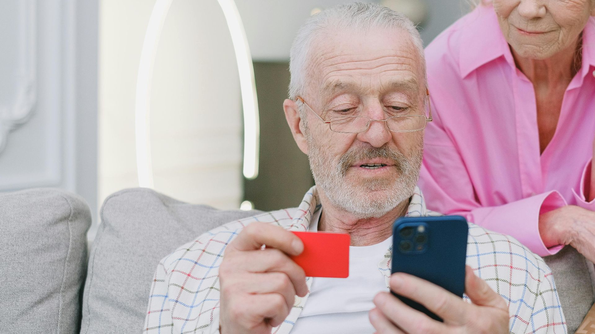 Elderly couple using smartphone and credit card for online shopping at home.