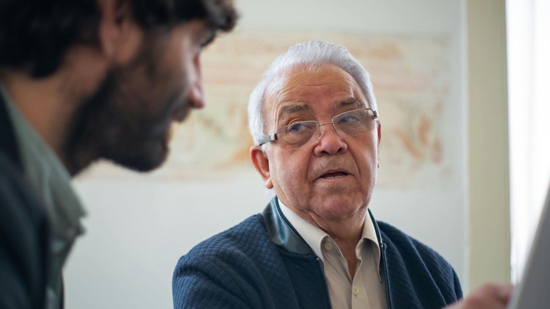 Elderly man with eyeglasses in a thoughtful discussion in Portugal indoors.