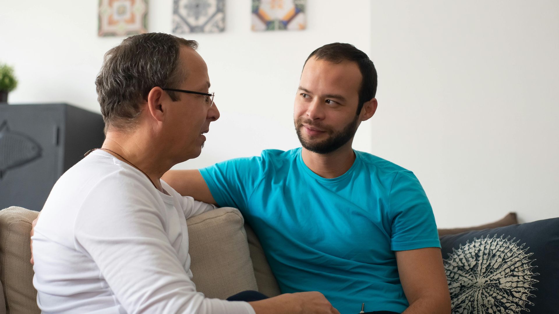 Two men share a heartfelt conversation on a cozy sofa in a modern living room.