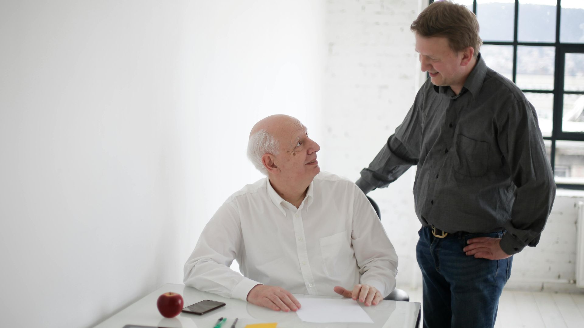 Positive men in different ages discussing project while working in loft styled workplace and looking at each other