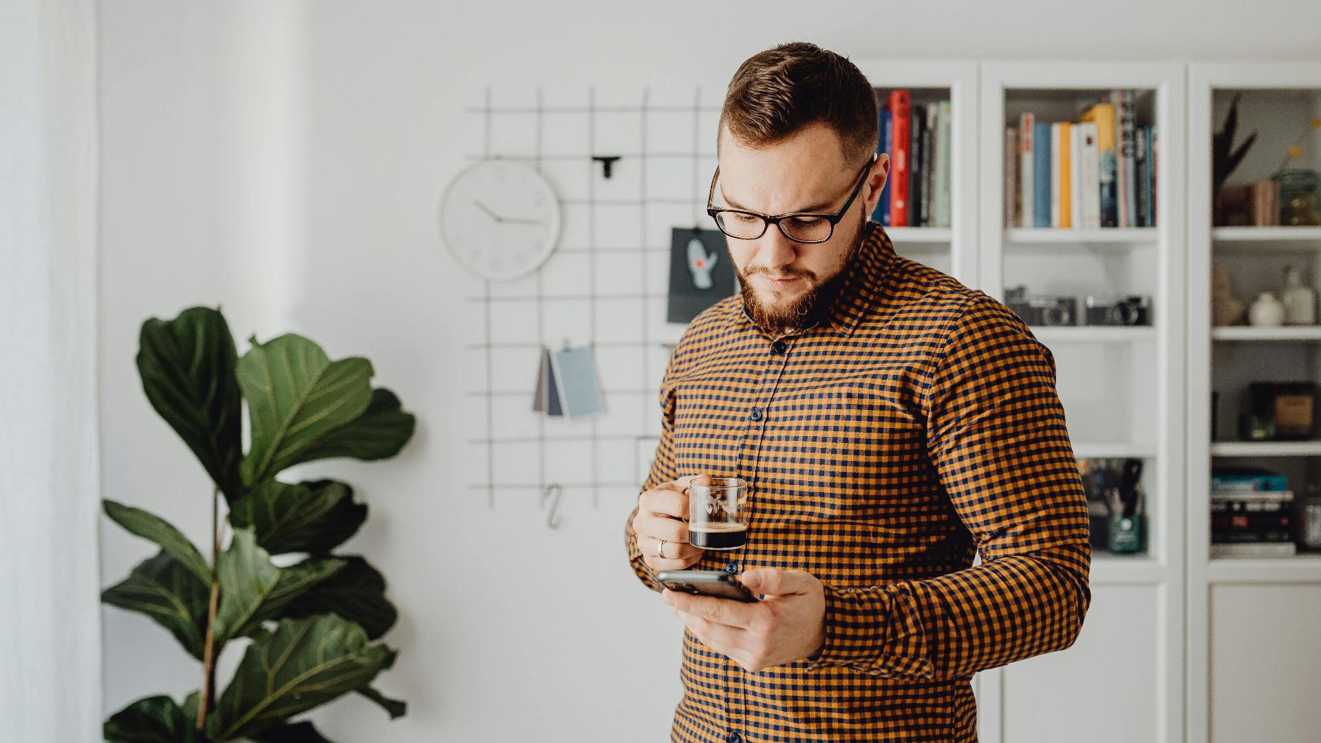Man enjoying coffee while browsing smartphone indoors, showcasing a modern lifestyle.