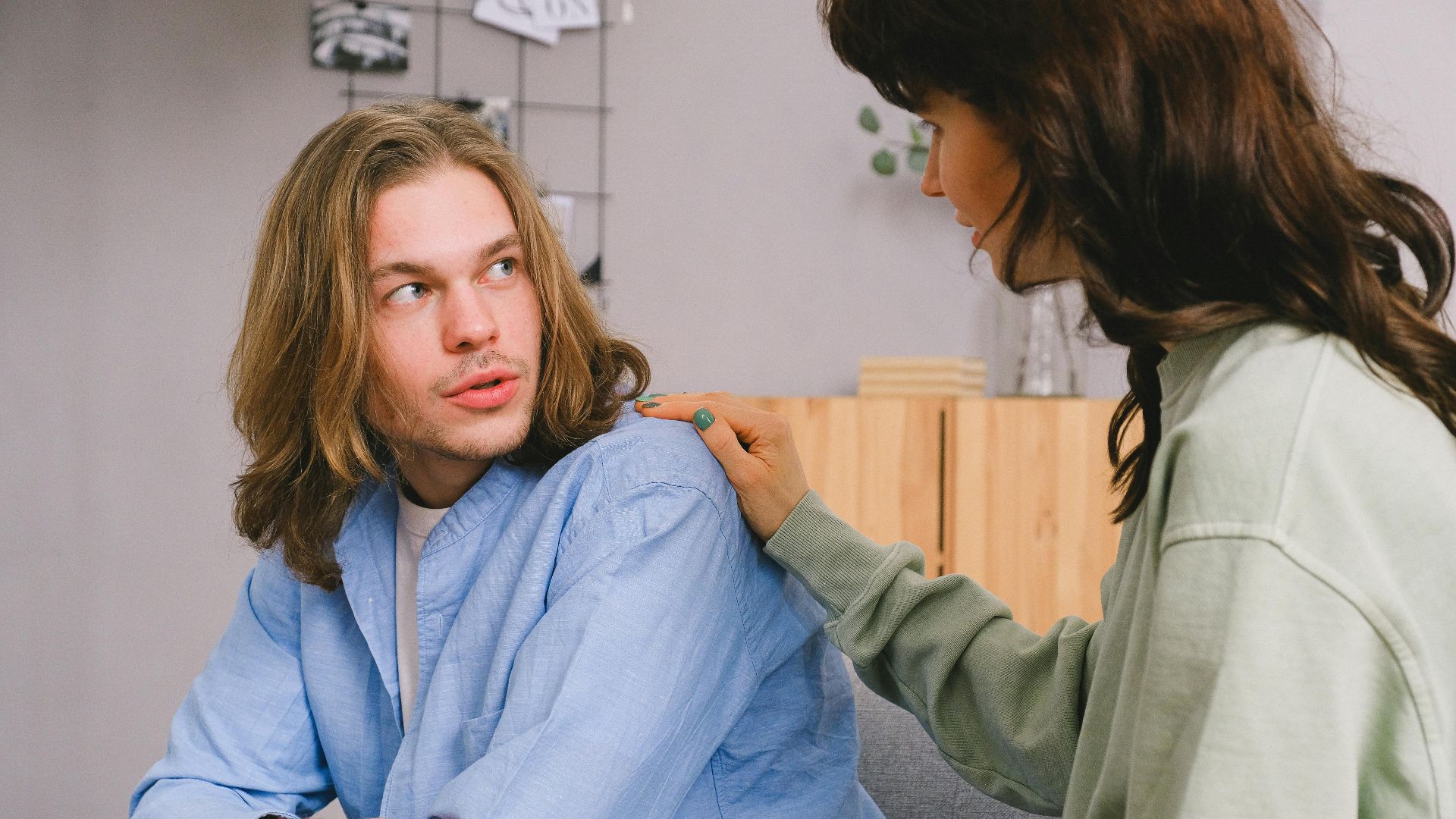Concentrated woman talking and touching shoulder of pensive male in light room in daytime