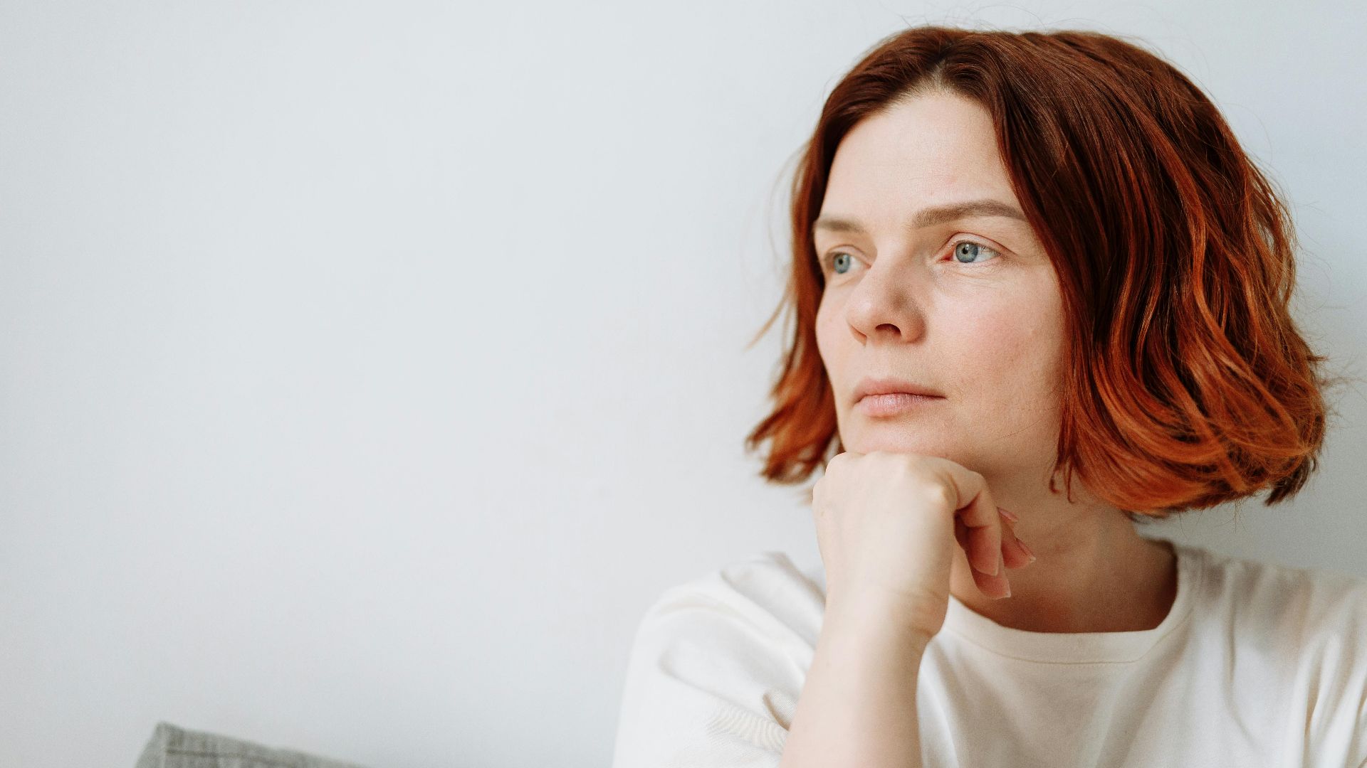 Pensive woman with red hair sitting indoors, conveying calm and contemplation.