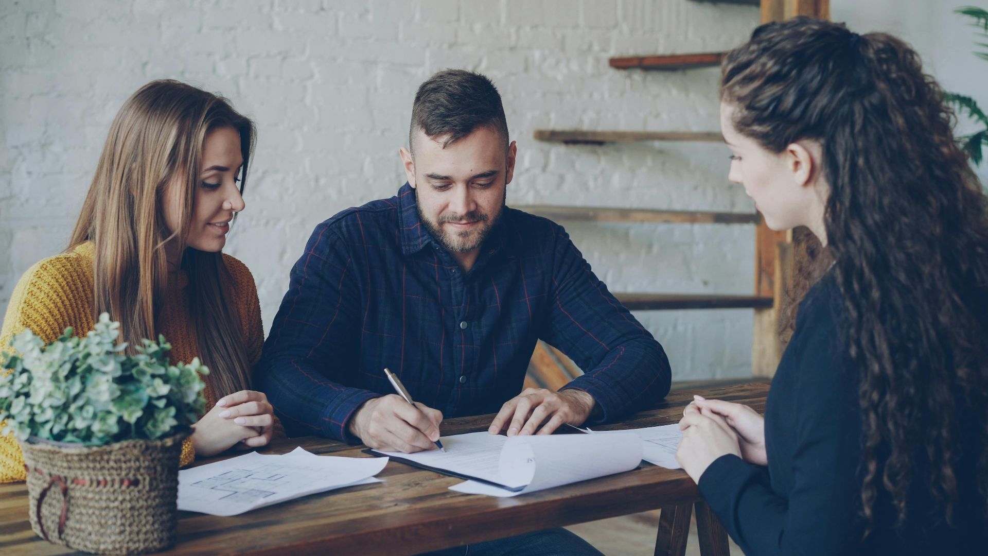 A young couple discussing paperwork with a real estate agent indoors.