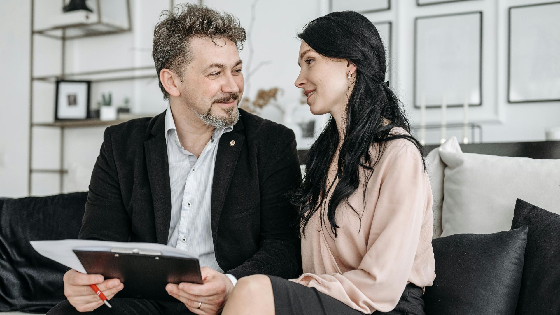 A couple sitting on a couch, smiling, and reviewing documents indoors.