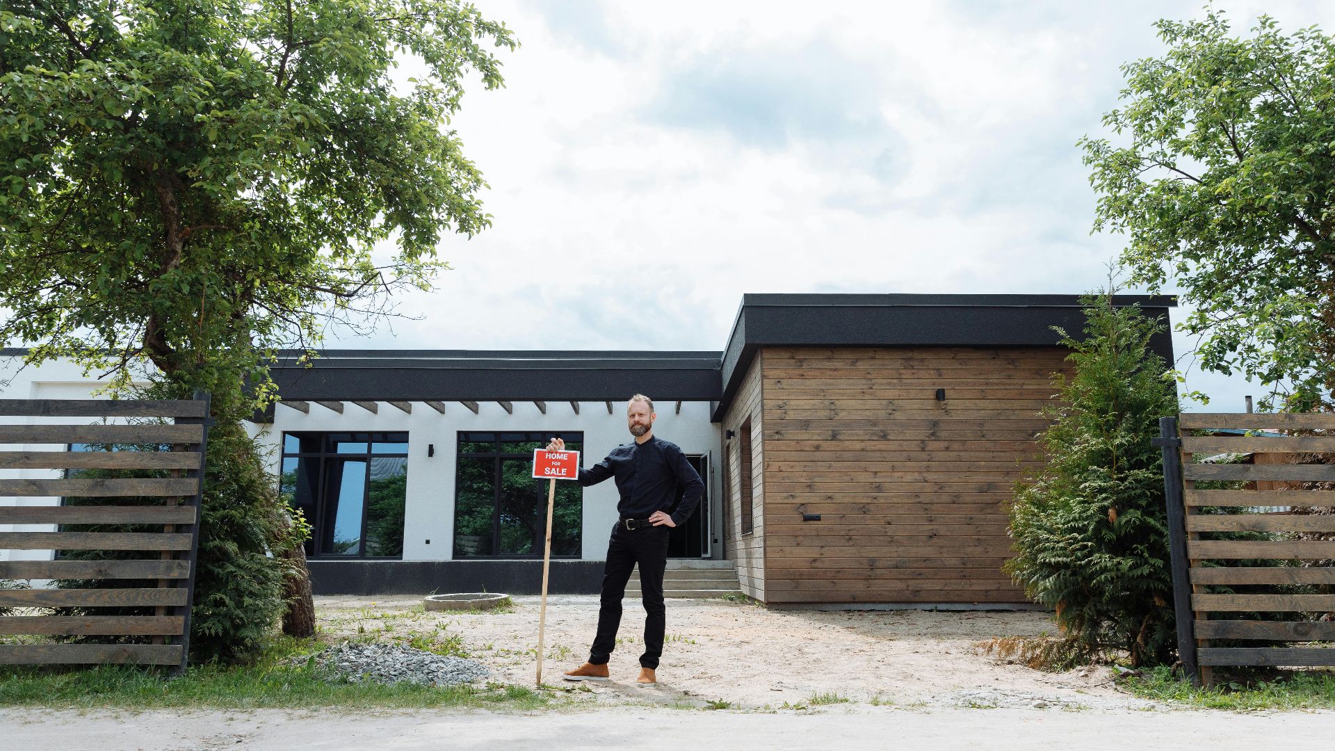 Real estate agent standing outside modern house with for sale sign, featuring contemporary design.