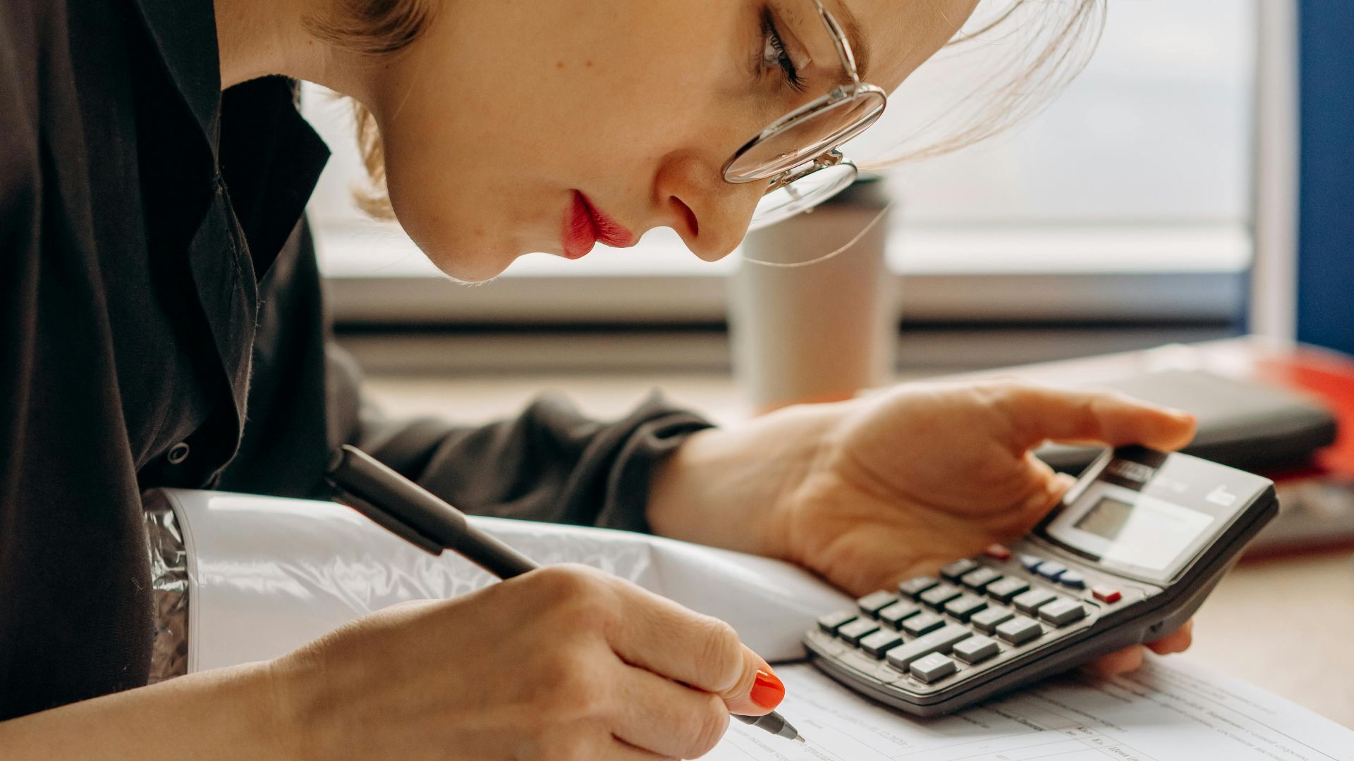 Woman with eyeglasses concentrating on financial calculations with notebook and calculator.