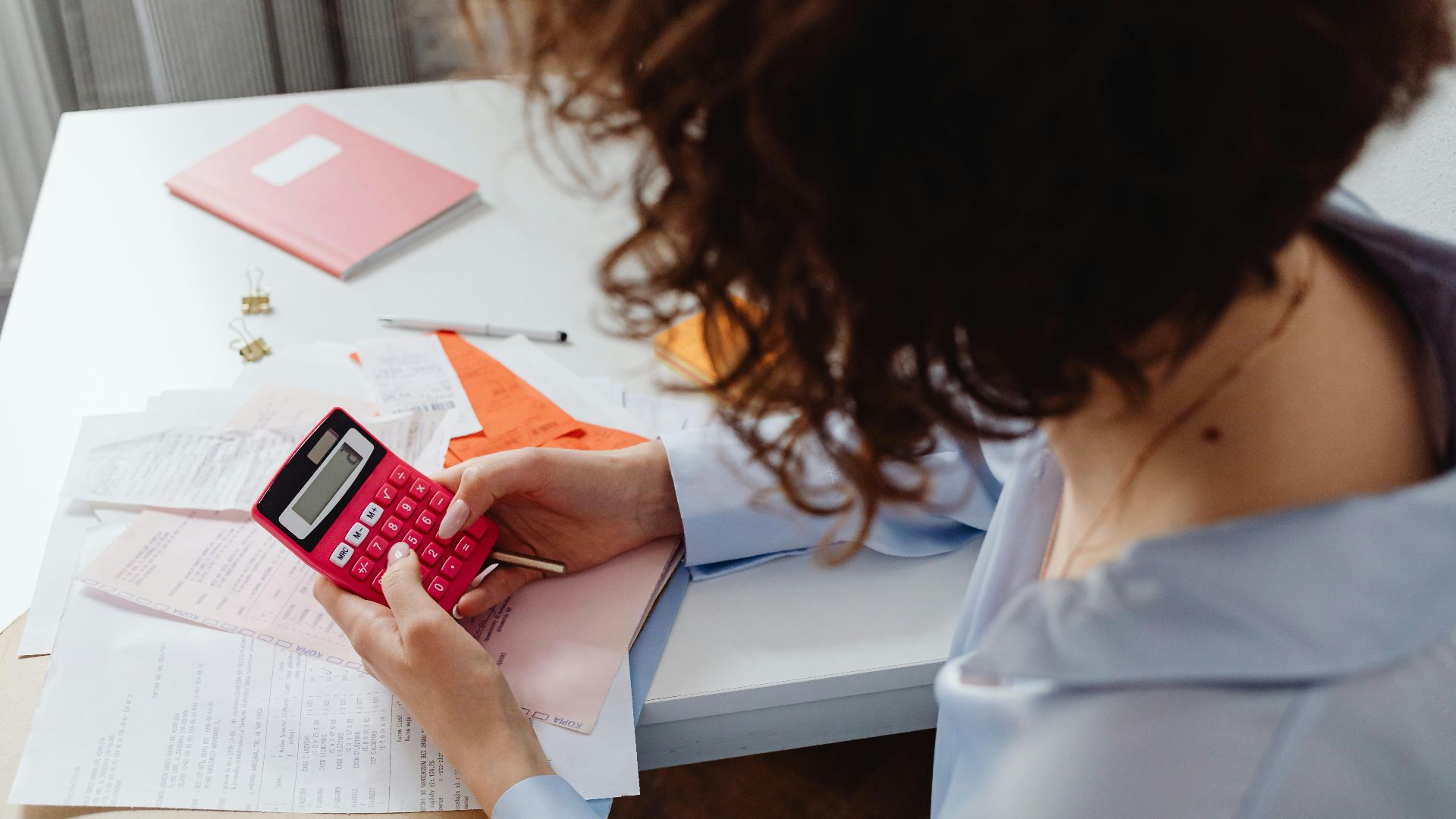 Woman calculating expenses with documents and calculator at work desk.
