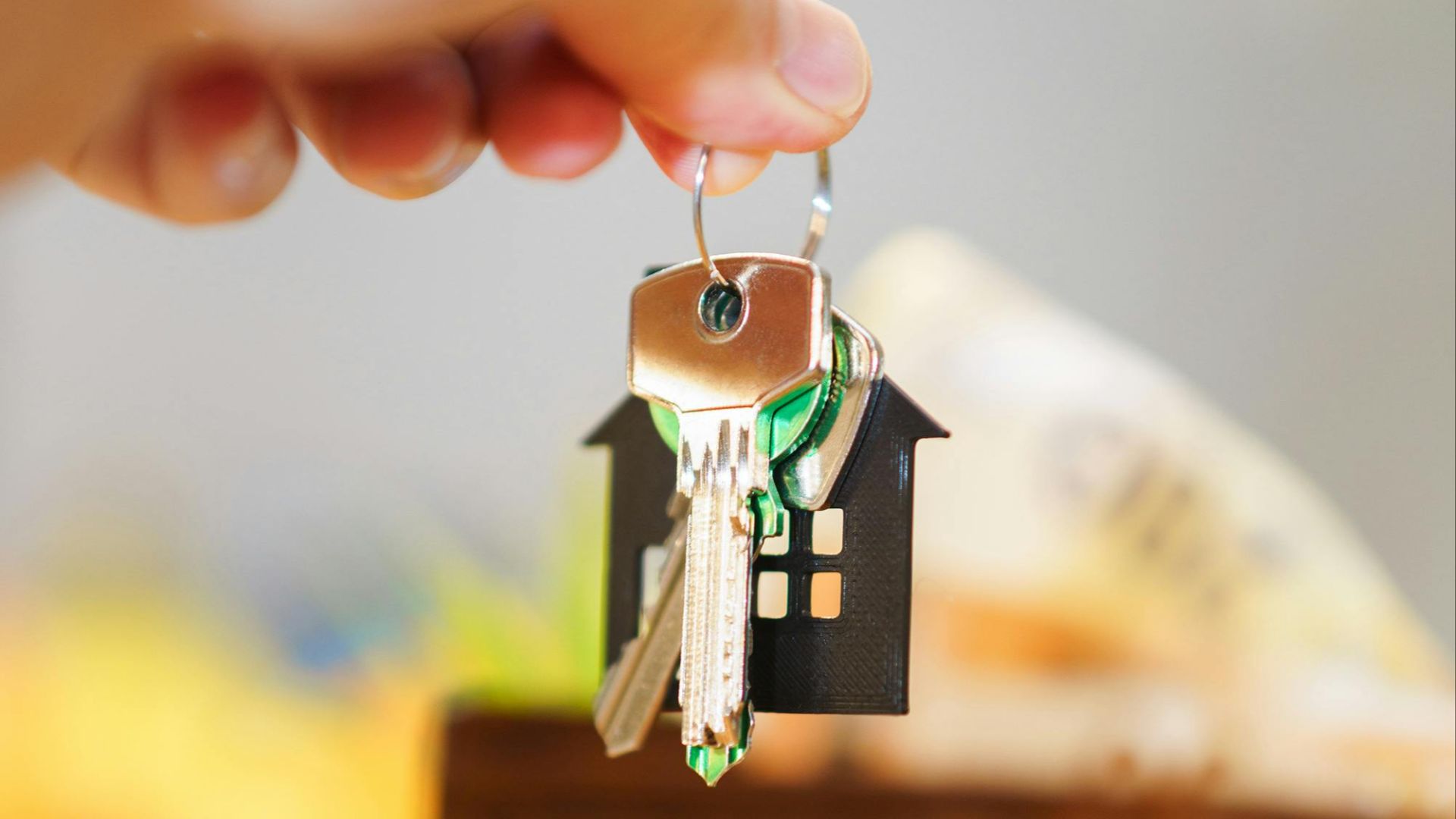 Hand holding house keys representing real estate investment with coins and wallet.