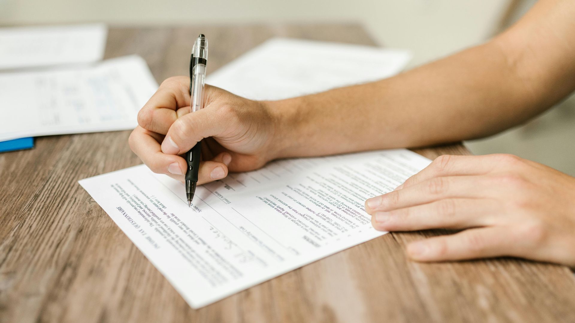Hand filling out paperwork with a pen, showcasing focus on document completion.