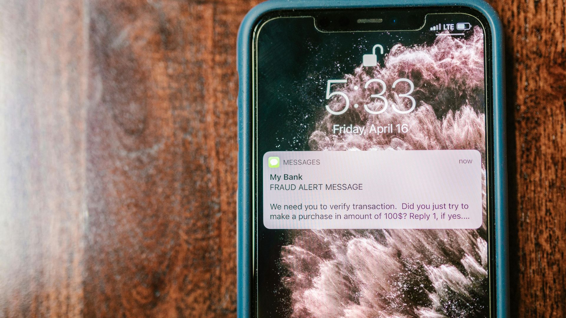 Close-up of a smartphone displaying a fraud alert notification on a wooden surface.