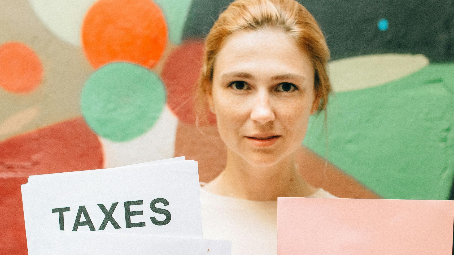 A professional woman holding tax documents and a 'Need Help?' sign, offering tax assistance.