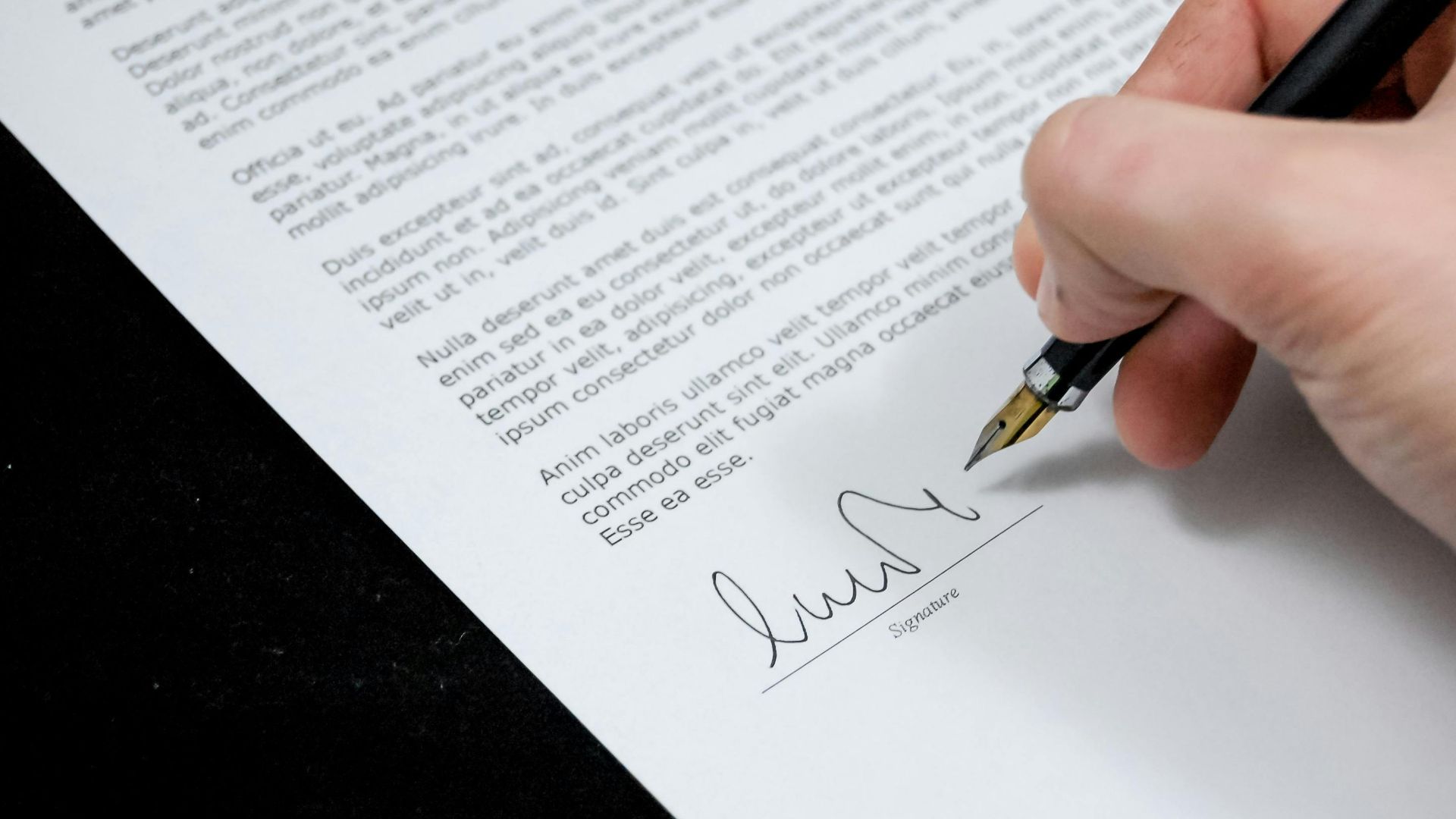 Close-up of a hand signing a formal document with a fountain pen, indicating agreement.