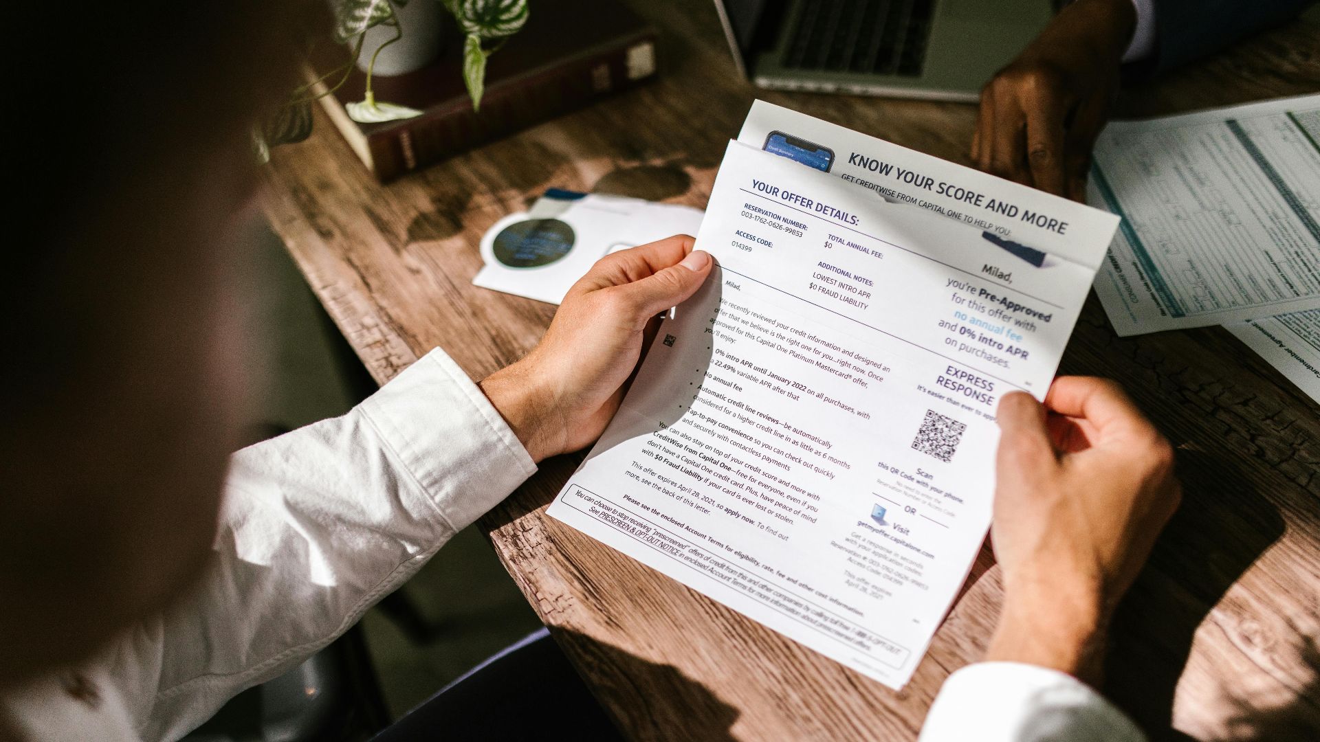 An adult man examining a financial document under natural light at a wooden desk, emphasizing finance and reading.