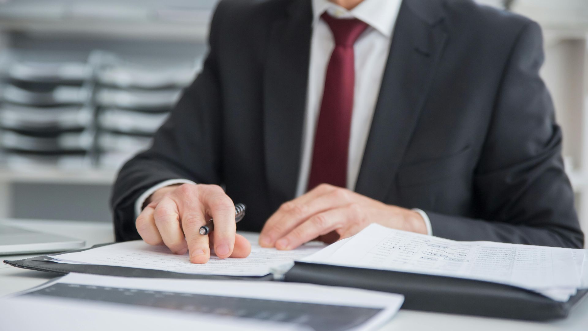 Close-up of a businessman reviewing documents at an office desk. Focus on hands and paperwork.