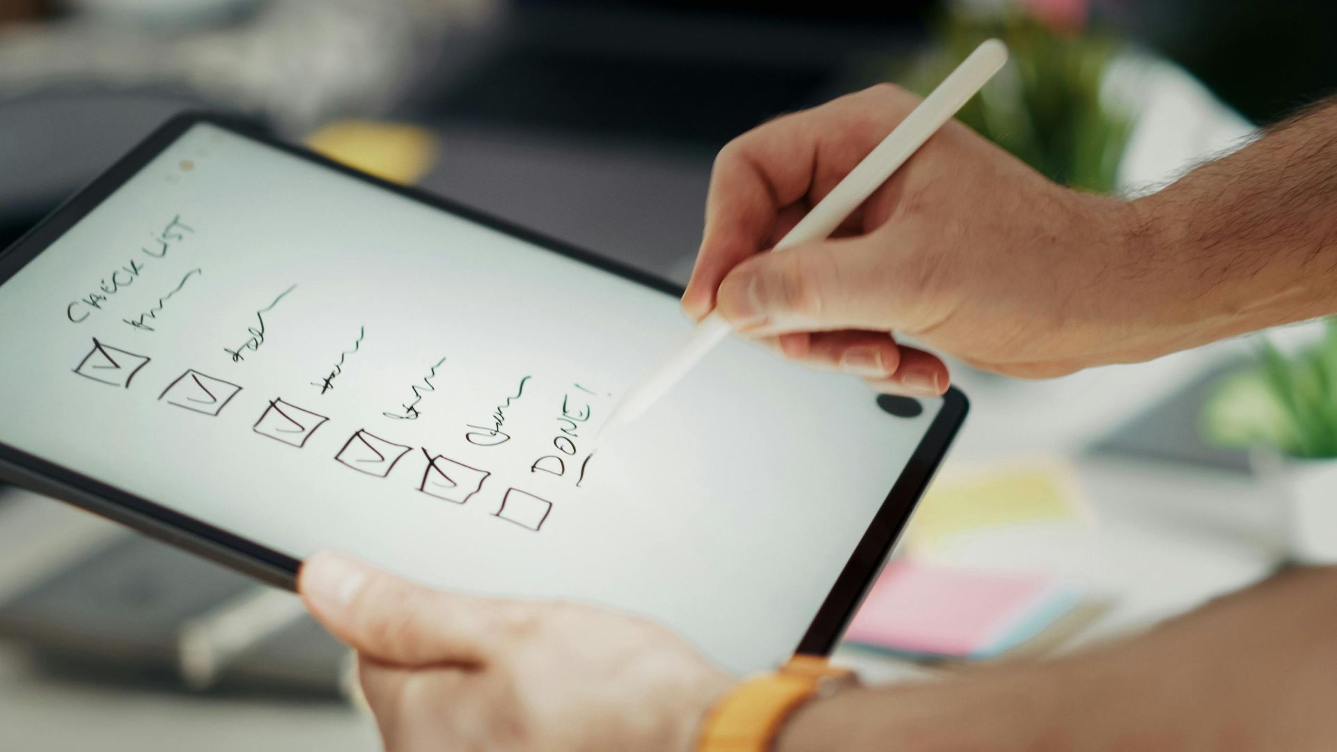 Close-up of a hand writing on a digital checklist using a stylus on a tablet, enhancing productivity.