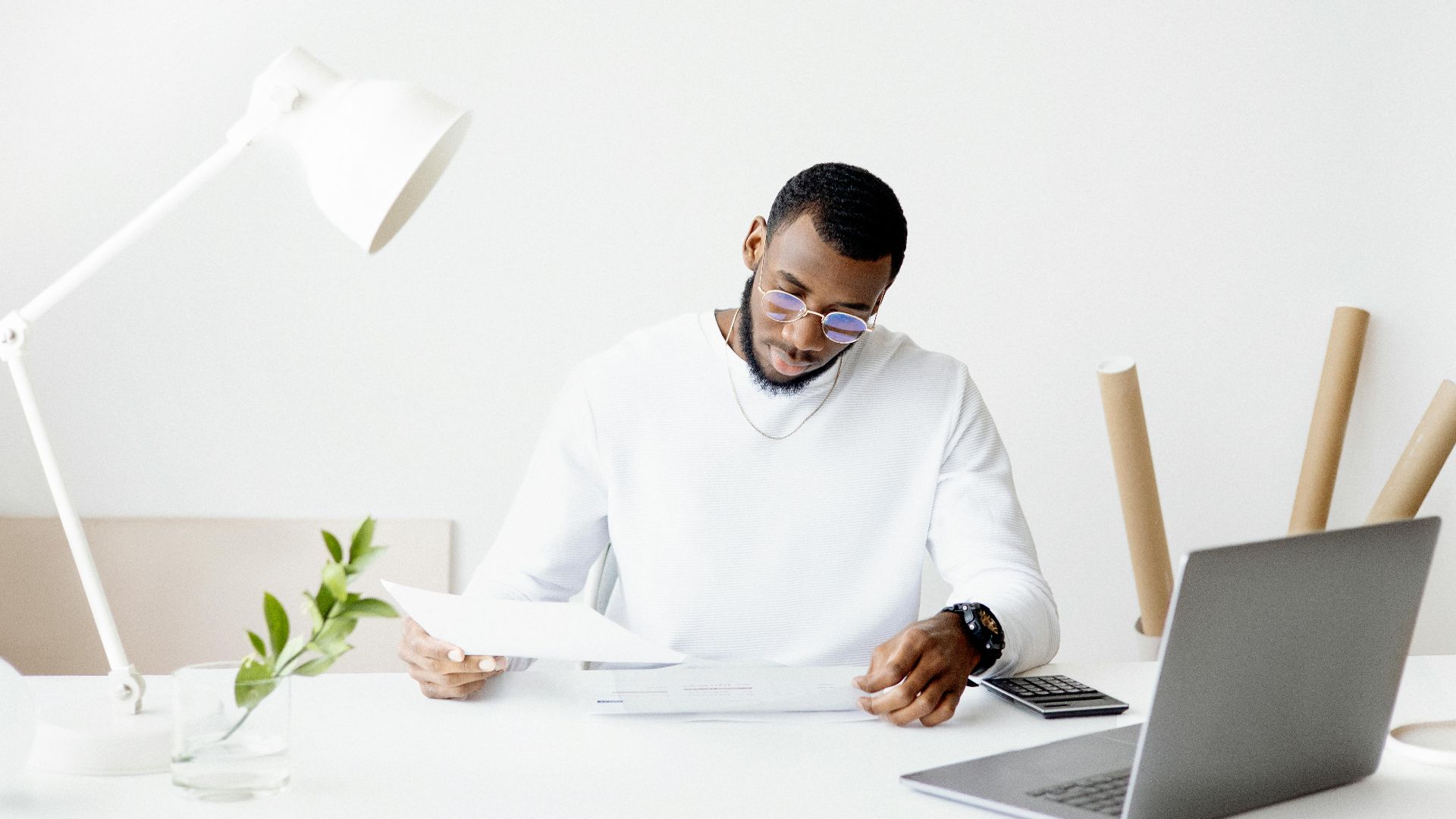 A professional adult working intently at a minimalist desk with a laptop, papers, and a lamp.