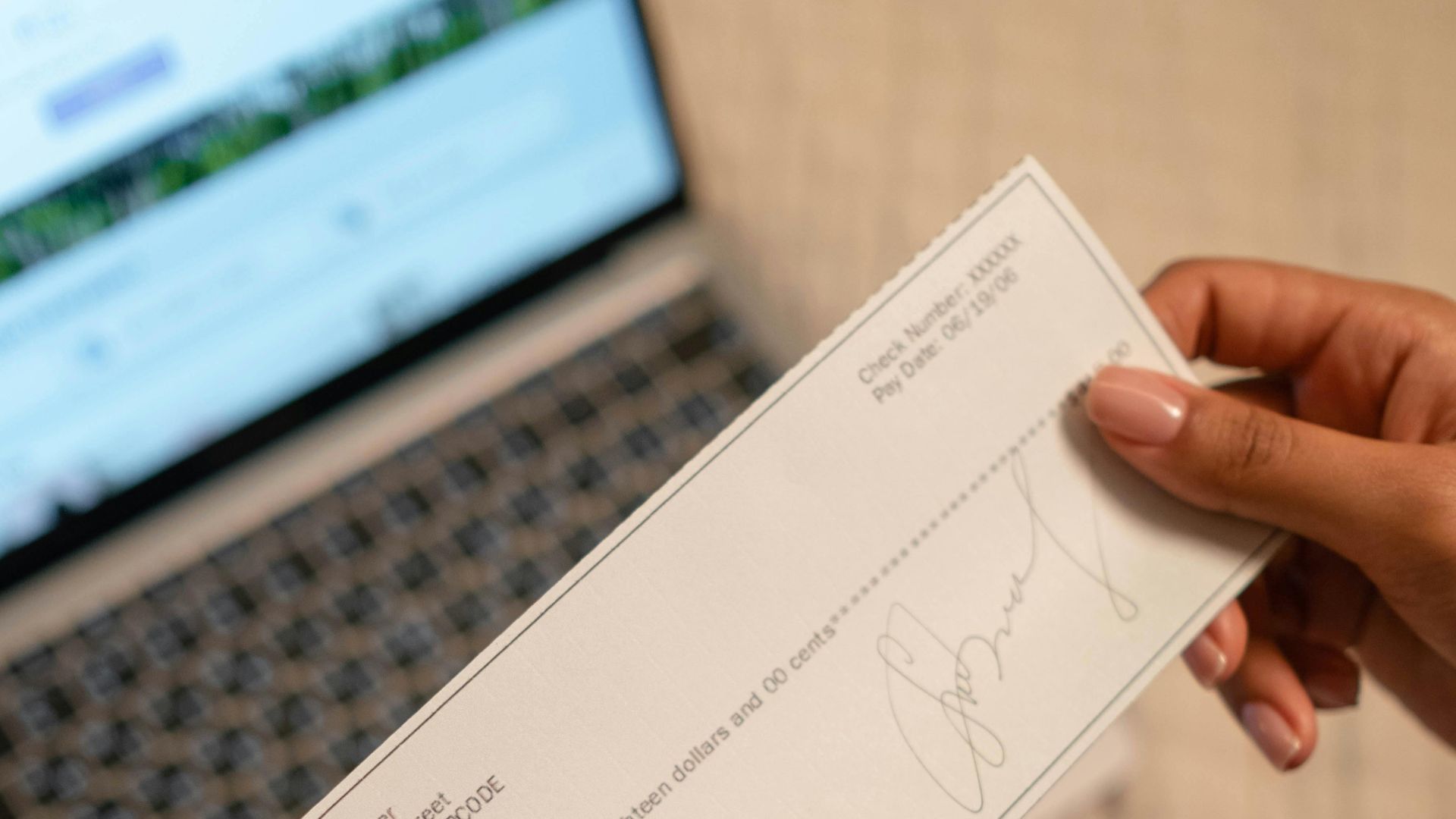 Individual holding a cheque over laptop, signifying online banking or financial transaction.