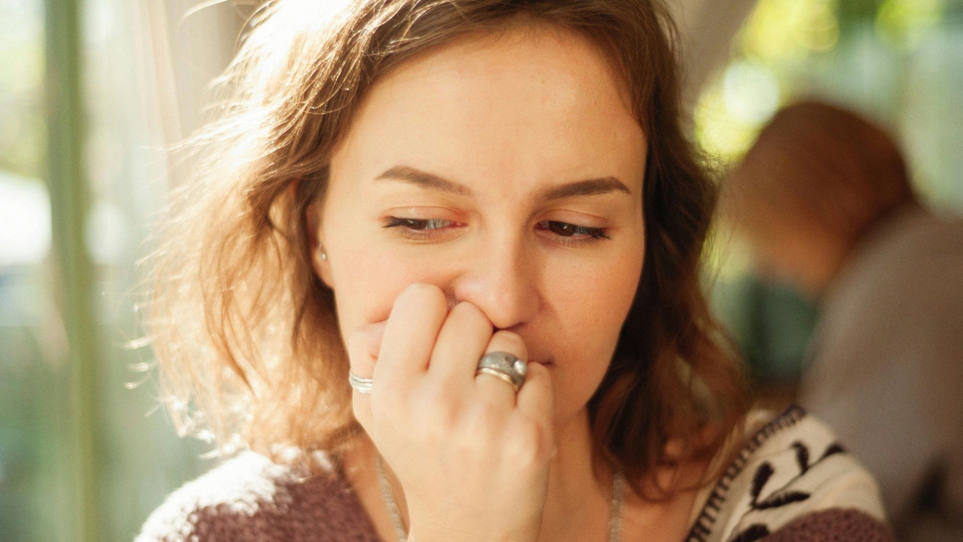 Thoughtful young woman posing indoors with hand on face.