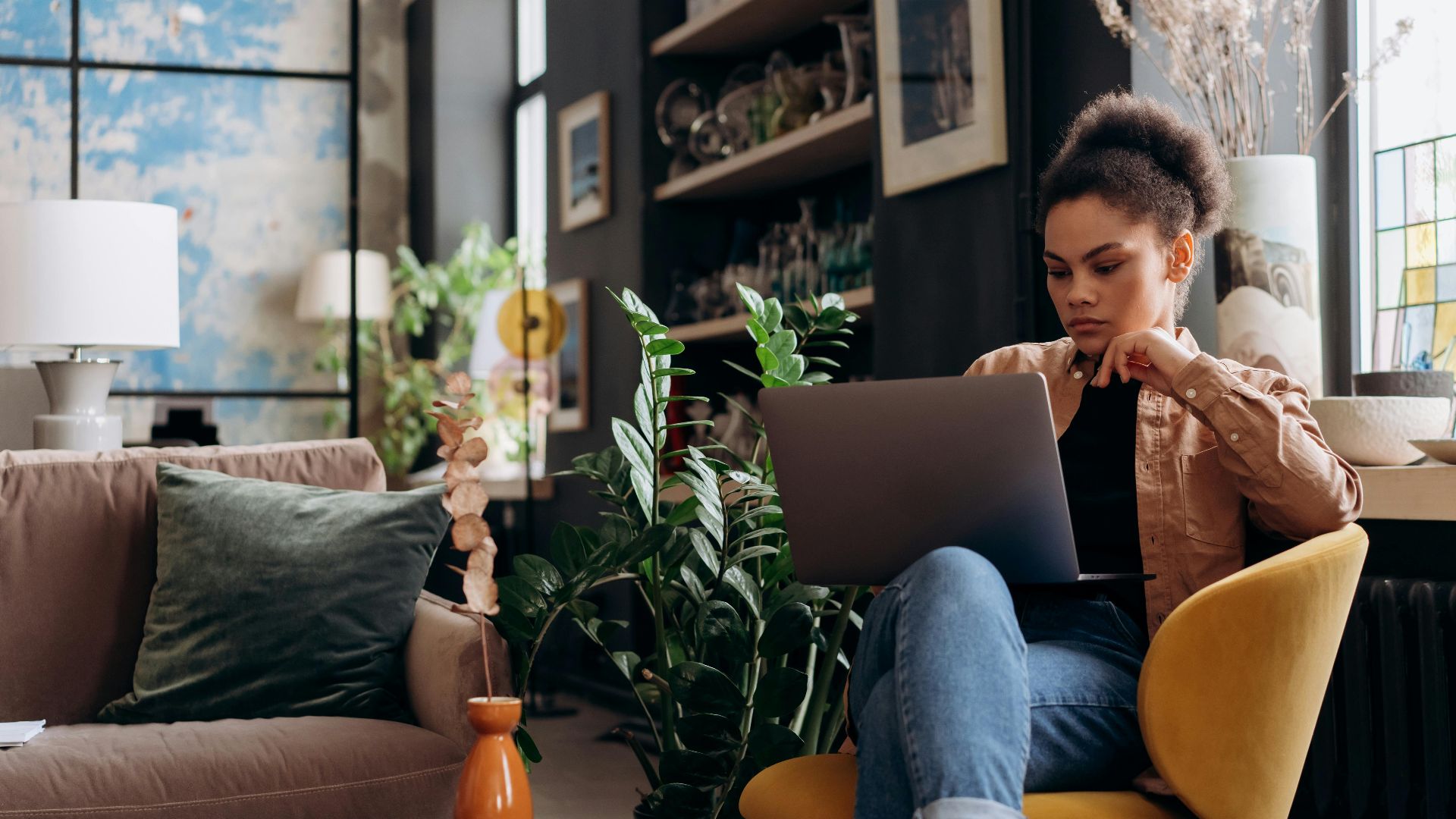 Focused woman working on laptop in a stylish home office environment, emphasizing a modern and relaxed work setting.
