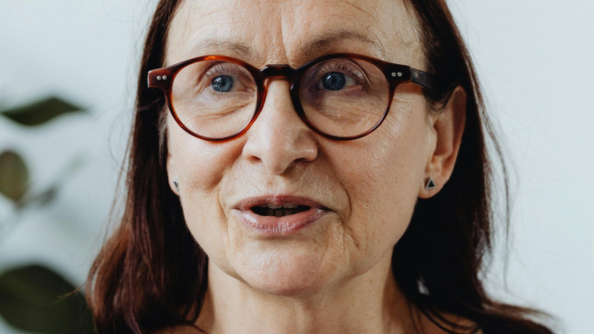 A thoughtful elderly woman wearing glasses, captured in a candid moment indoors.